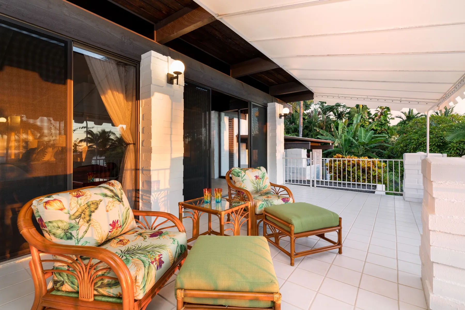 A covered patio with cushioned seating overlooks a leafy garden.