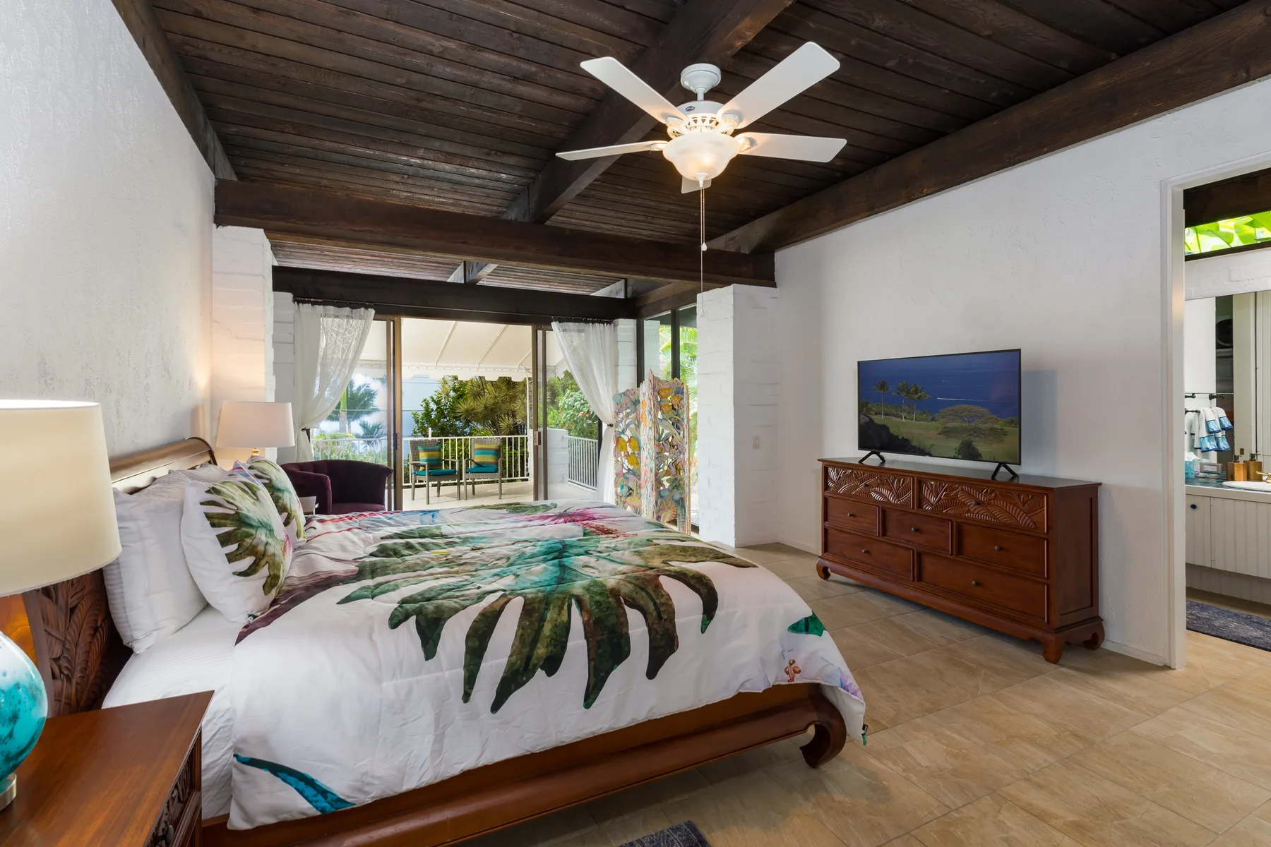 A bedroom with a large bed, ceiling fan, and sliding glass doors opening to a balcony.