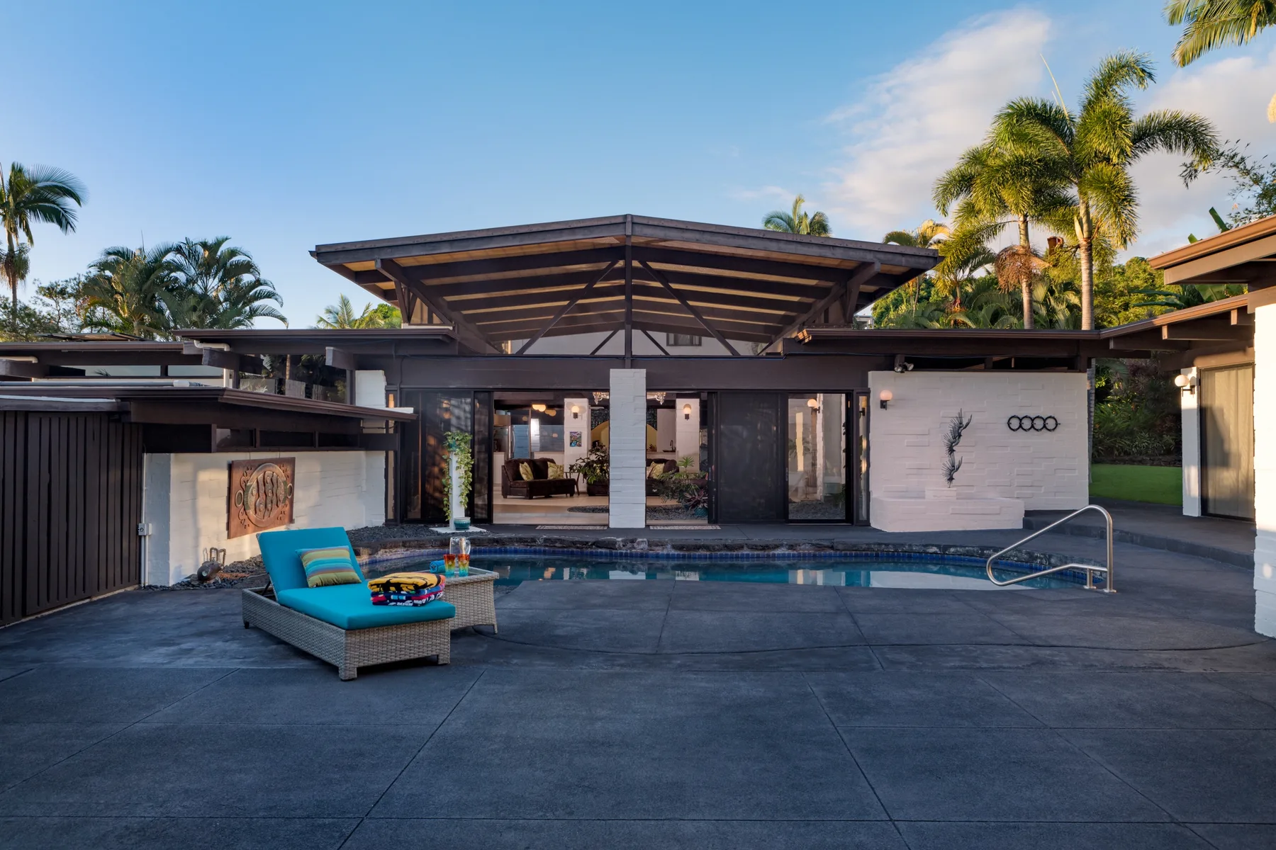 A modern house opens onto a patio with a swimming pool and lounge seating.