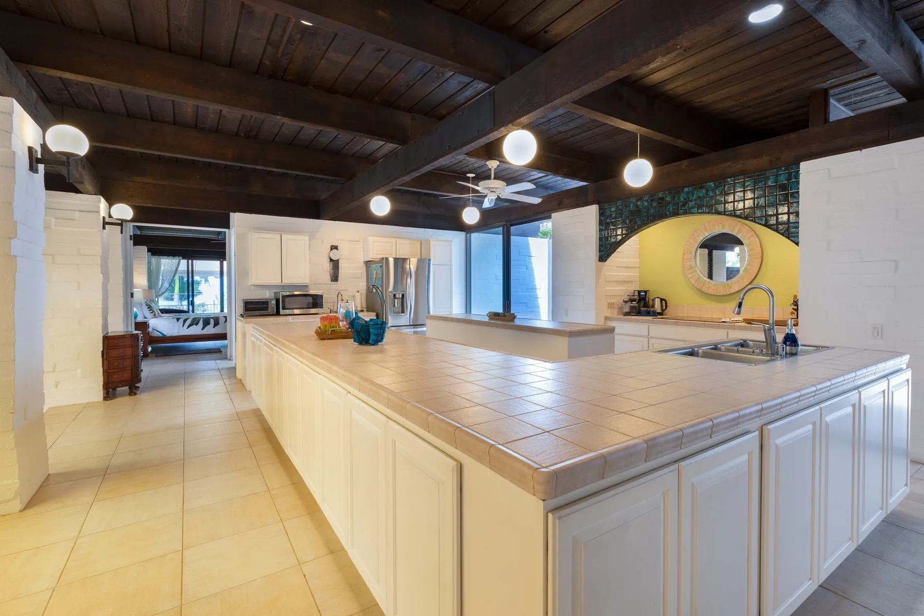 A spacious kitchen with a large island and a round mirror on the yellow wall.