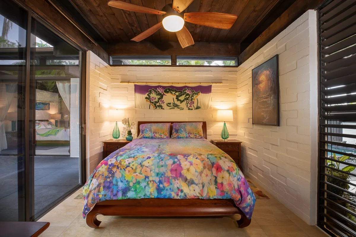 A bedroom with a colorful floral bedspread, bedside tables, and a ceiling fan.