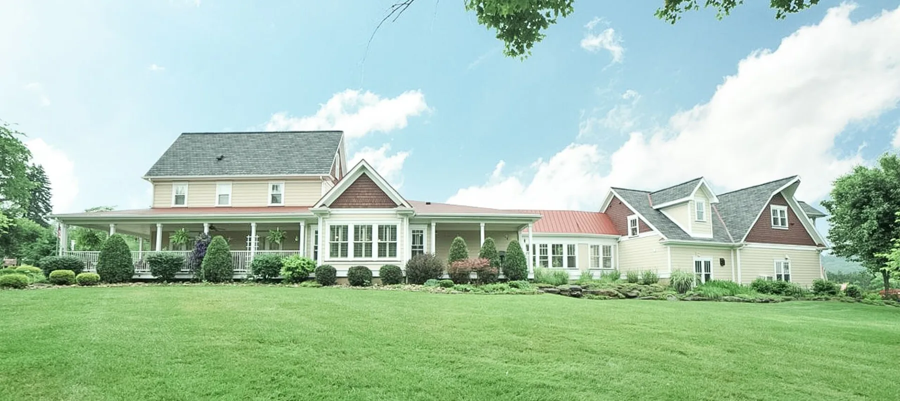 Home with yellow siding, wraparound porch and landscaped lawn
