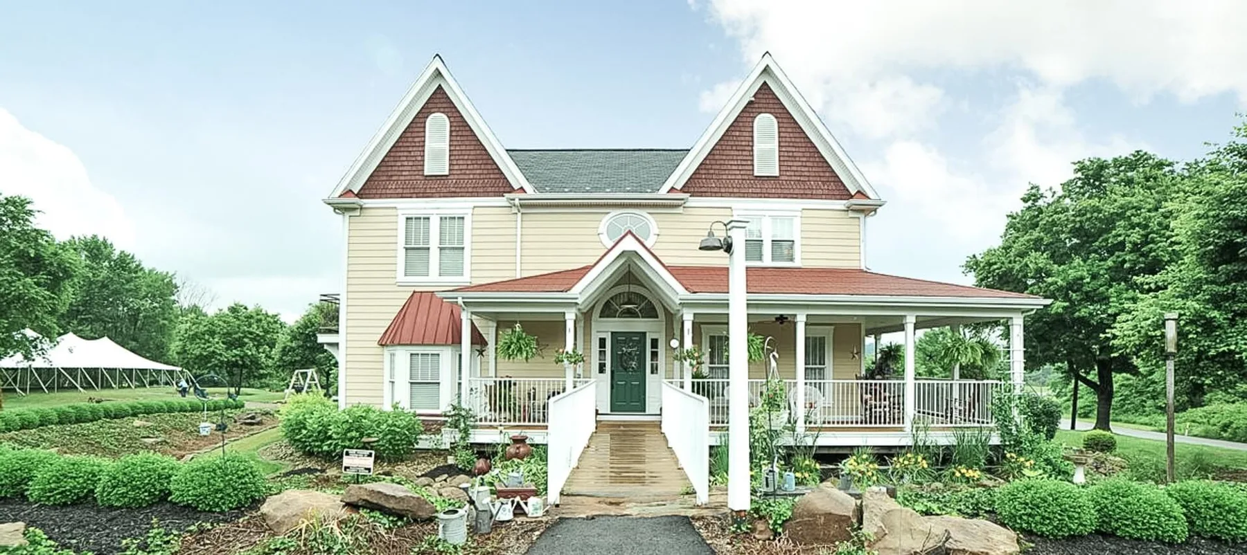 Yellow and red home with a wraparound porch, trees and landscaping
