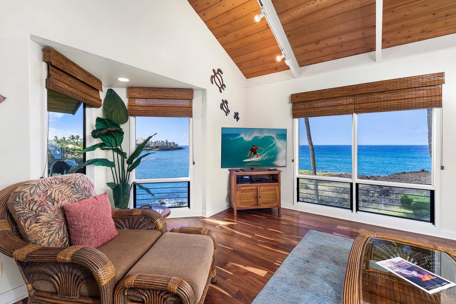 A bright living room with broad windows overlooking the ocean and a wooden ceiling.