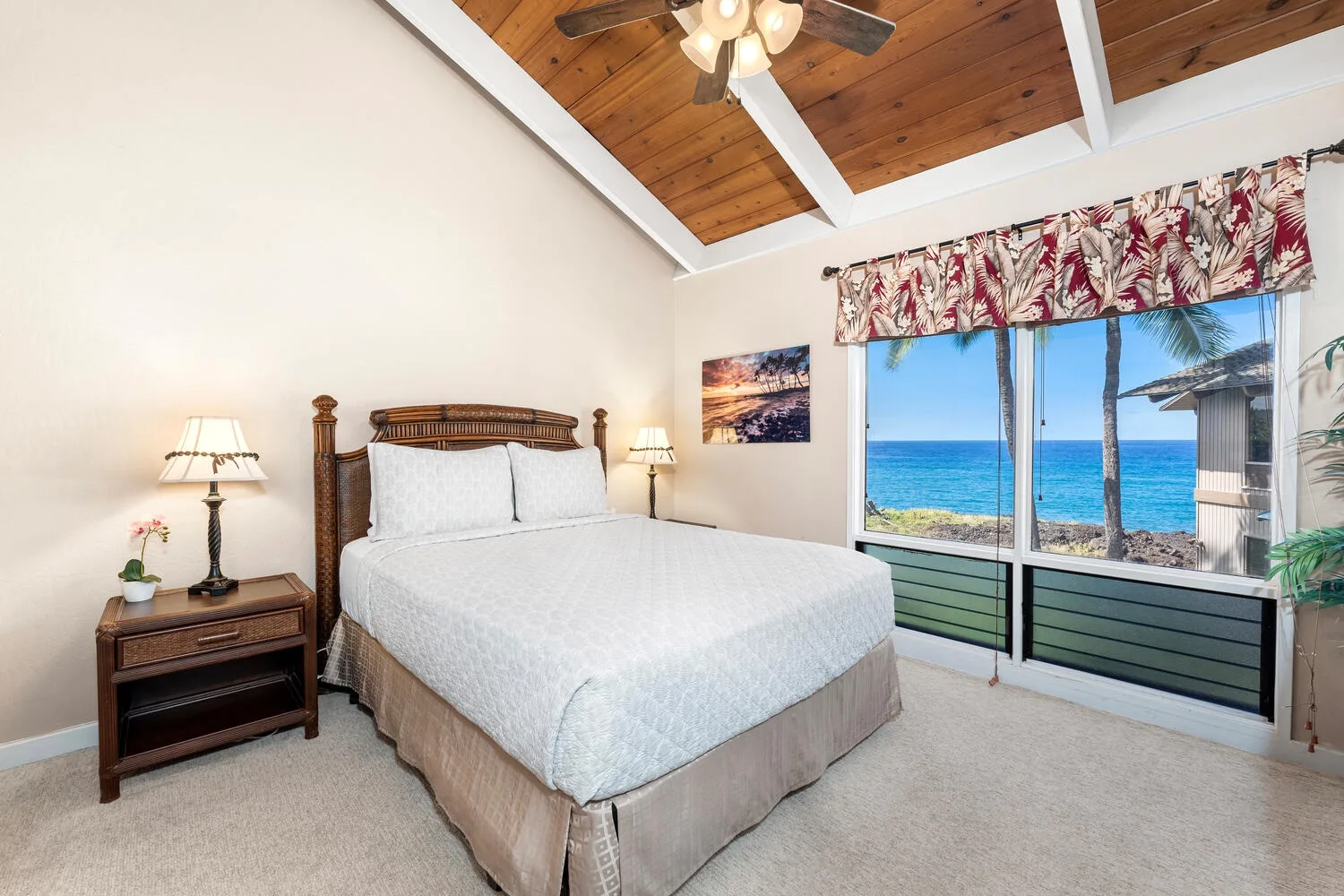 A bedroom with a bed beside large windows overlooking the ocean.