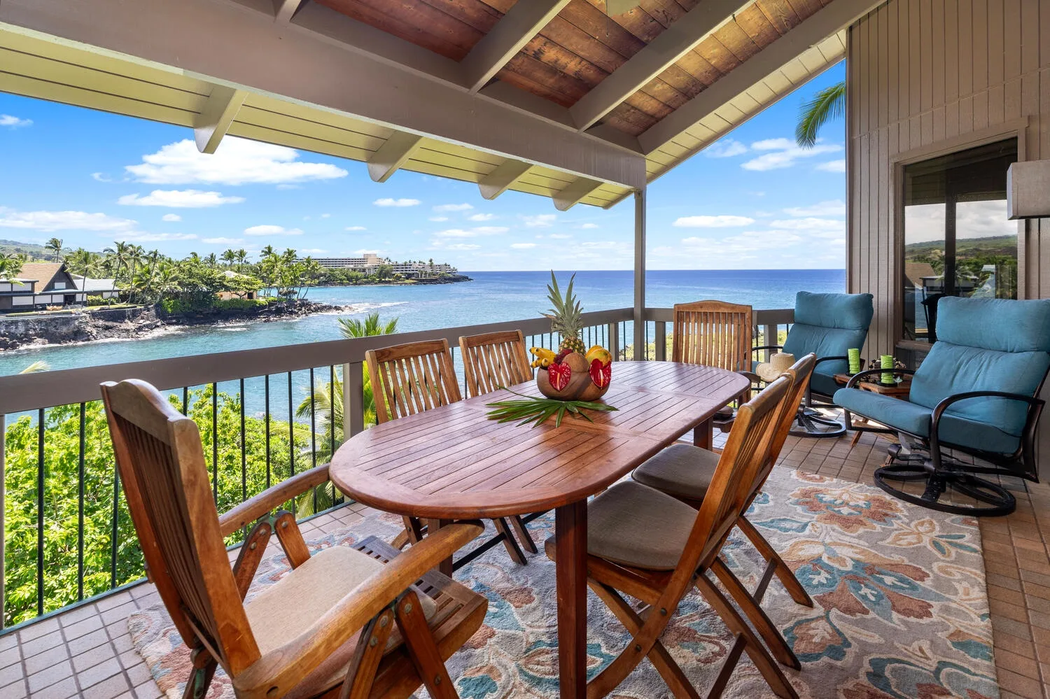 A covered seaside patio has a wooden dining table and seating overlooking the water.