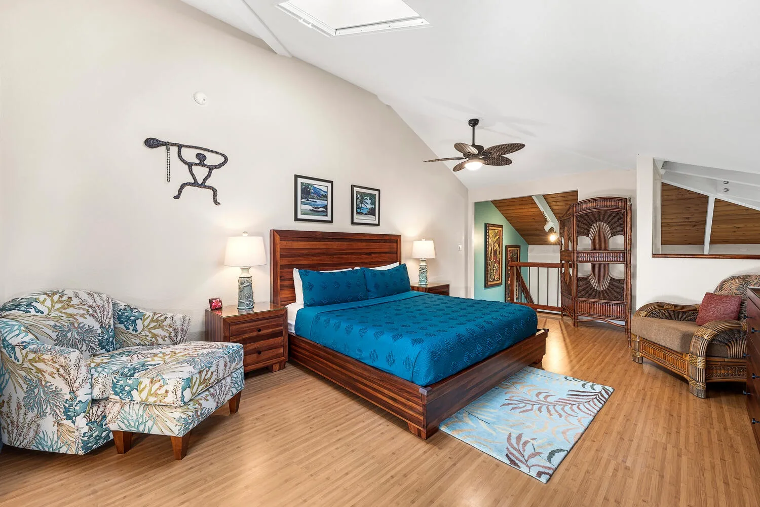 A bedroom with a blue bed, floral seating, and a ceiling fan.