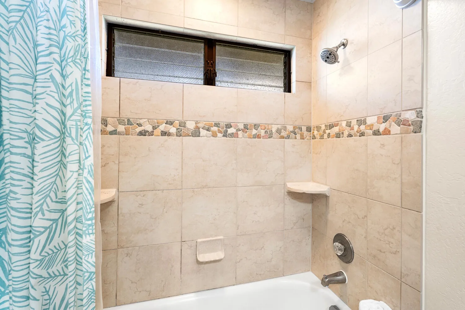 A tiled bathroom shower with a patterned curtain and a narrow window.