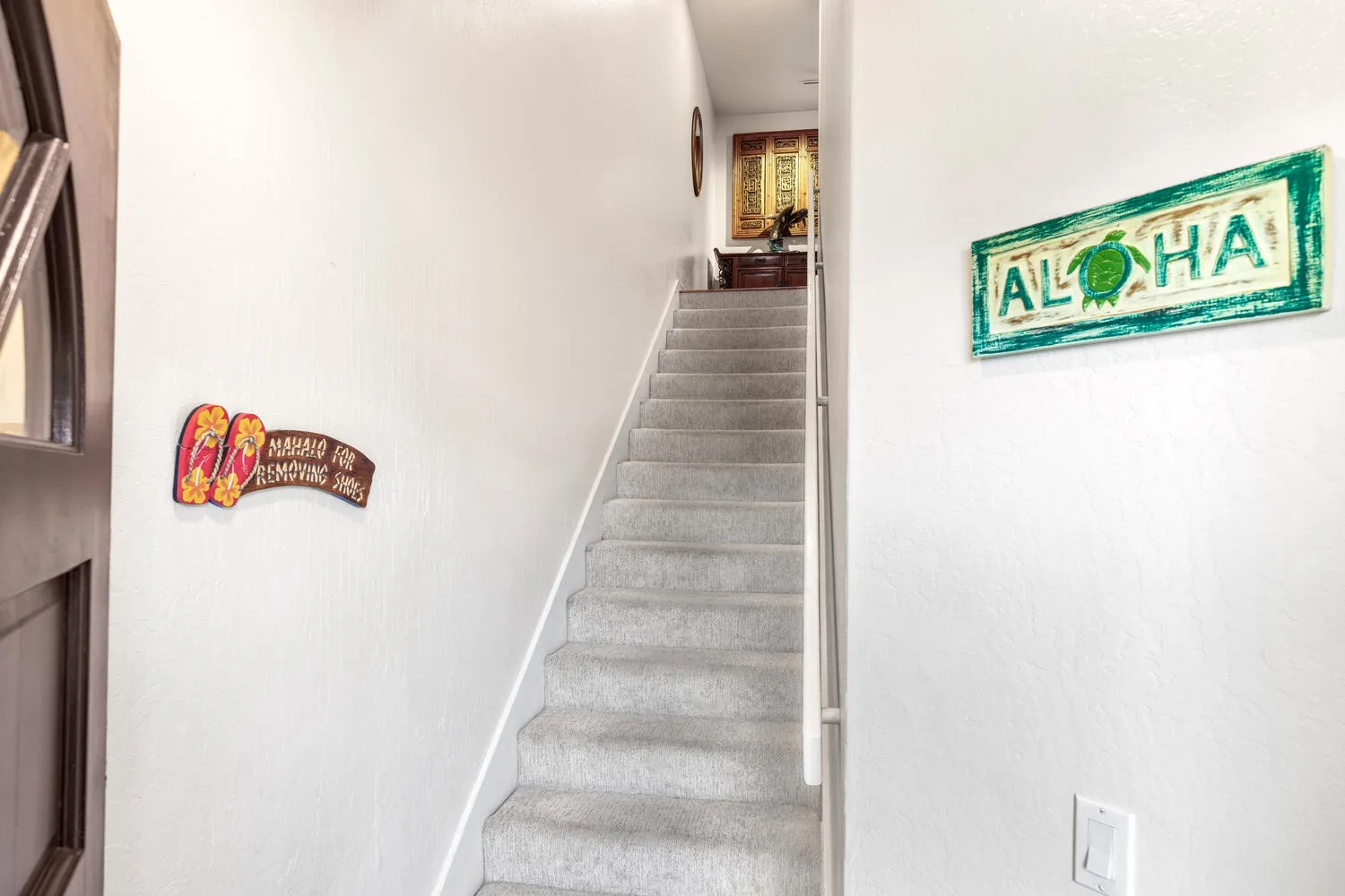 A carpeted staircase rises between white walls with decorative signs.