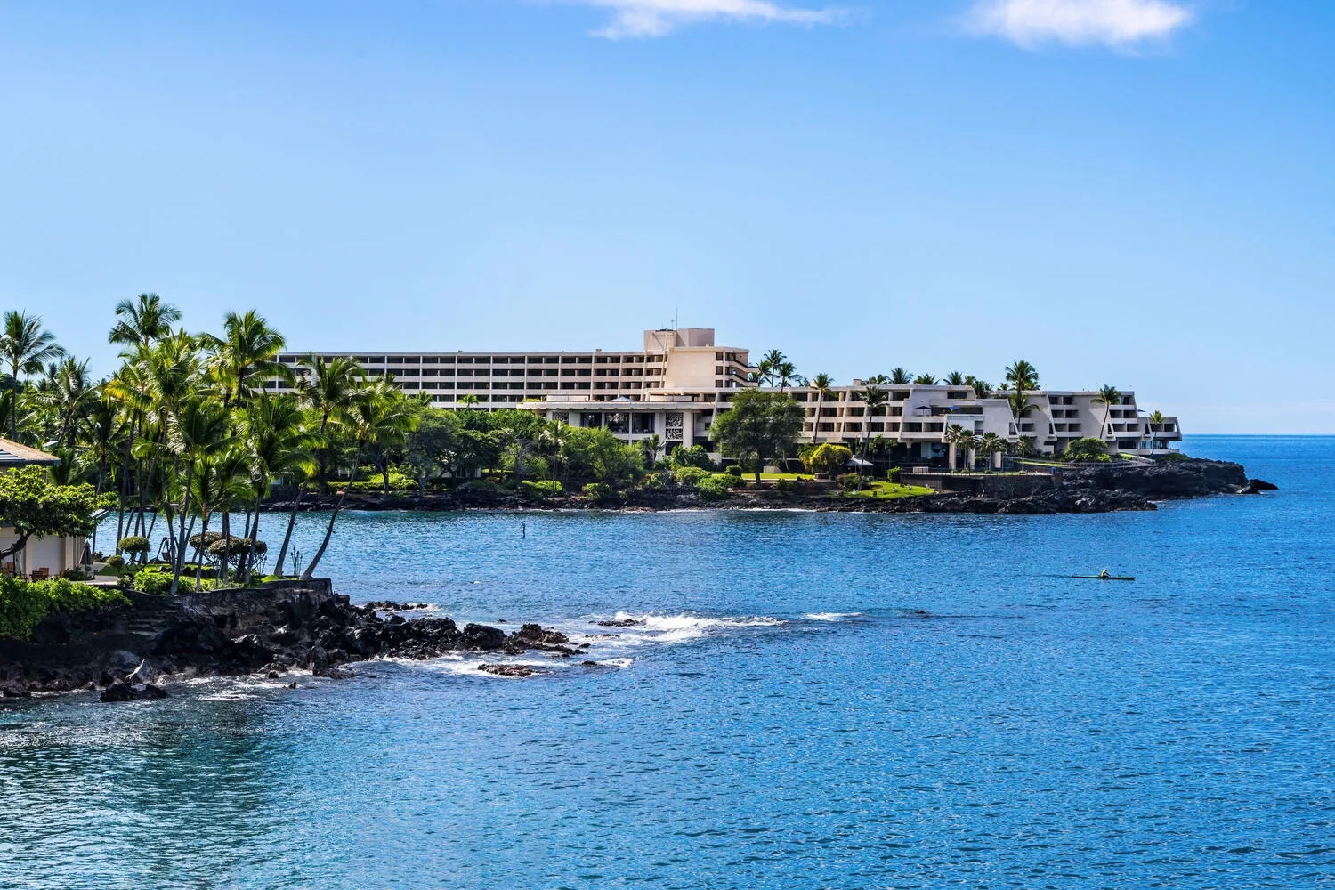 A coastal resort building overlooks a rocky shoreline and blue water.