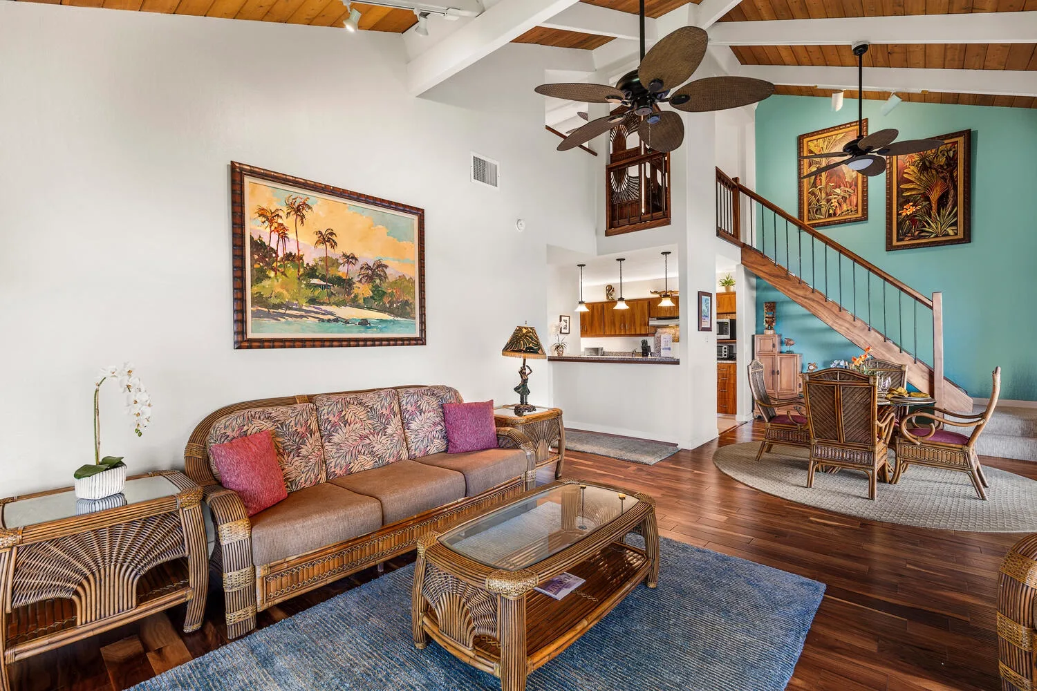 A bright living room has woven seating, a blue rug, and an open view to the kitchen.