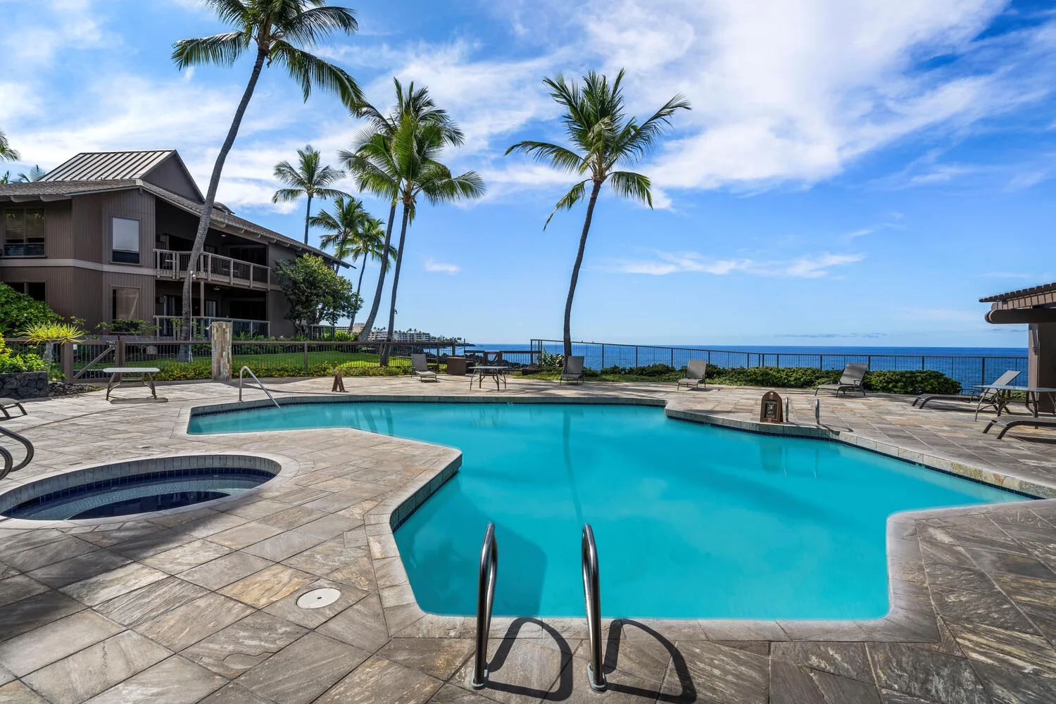 An outdoor swimming pool beside a palm-lined patio, with the ocean visible beyond.