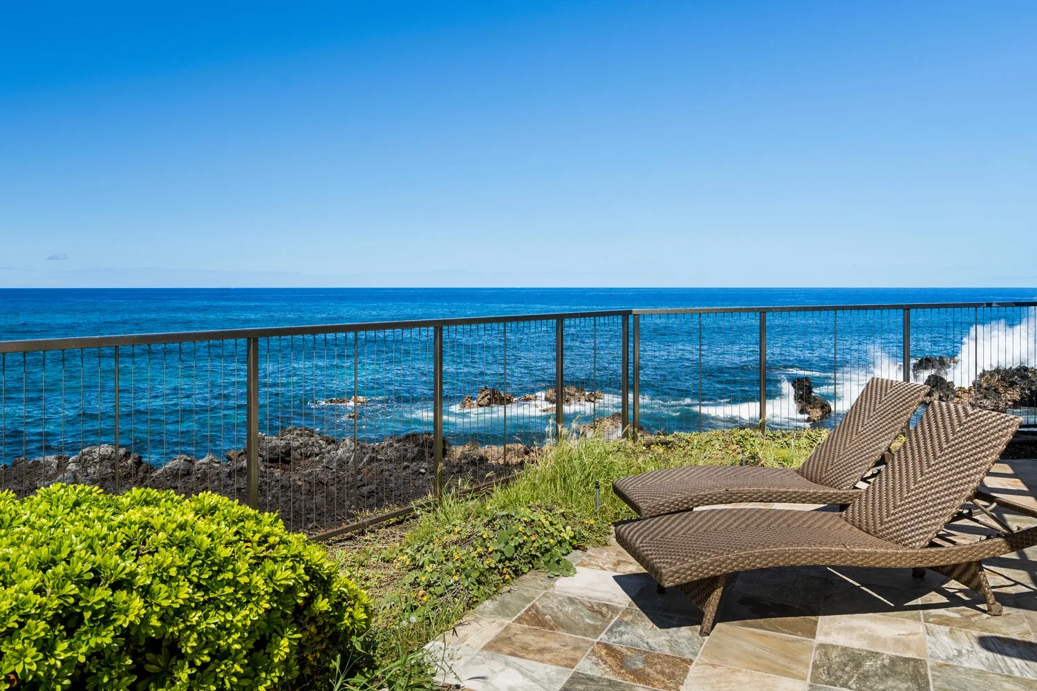 A seaside patio with reclining seating overlooks the ocean.