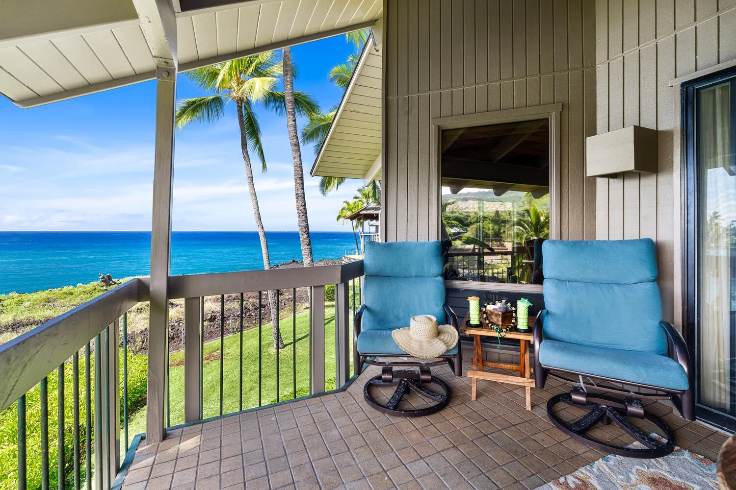 A covered balcony overlooks the ocean, with blue seating beside the railing.