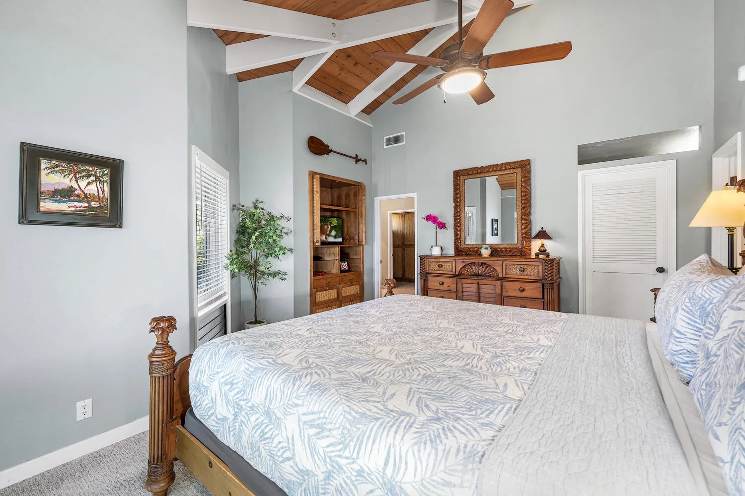 A bedroom with a large bed, wooden dresser, and vaulted wood ceiling.