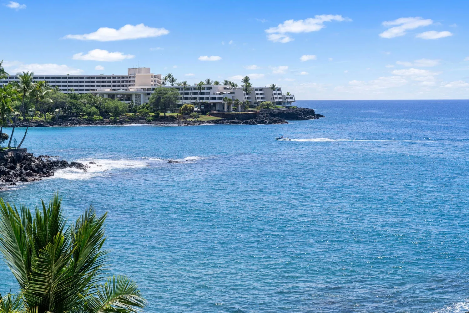 Coastal resort buildings overlook blue ocean water and a rocky shoreline.
