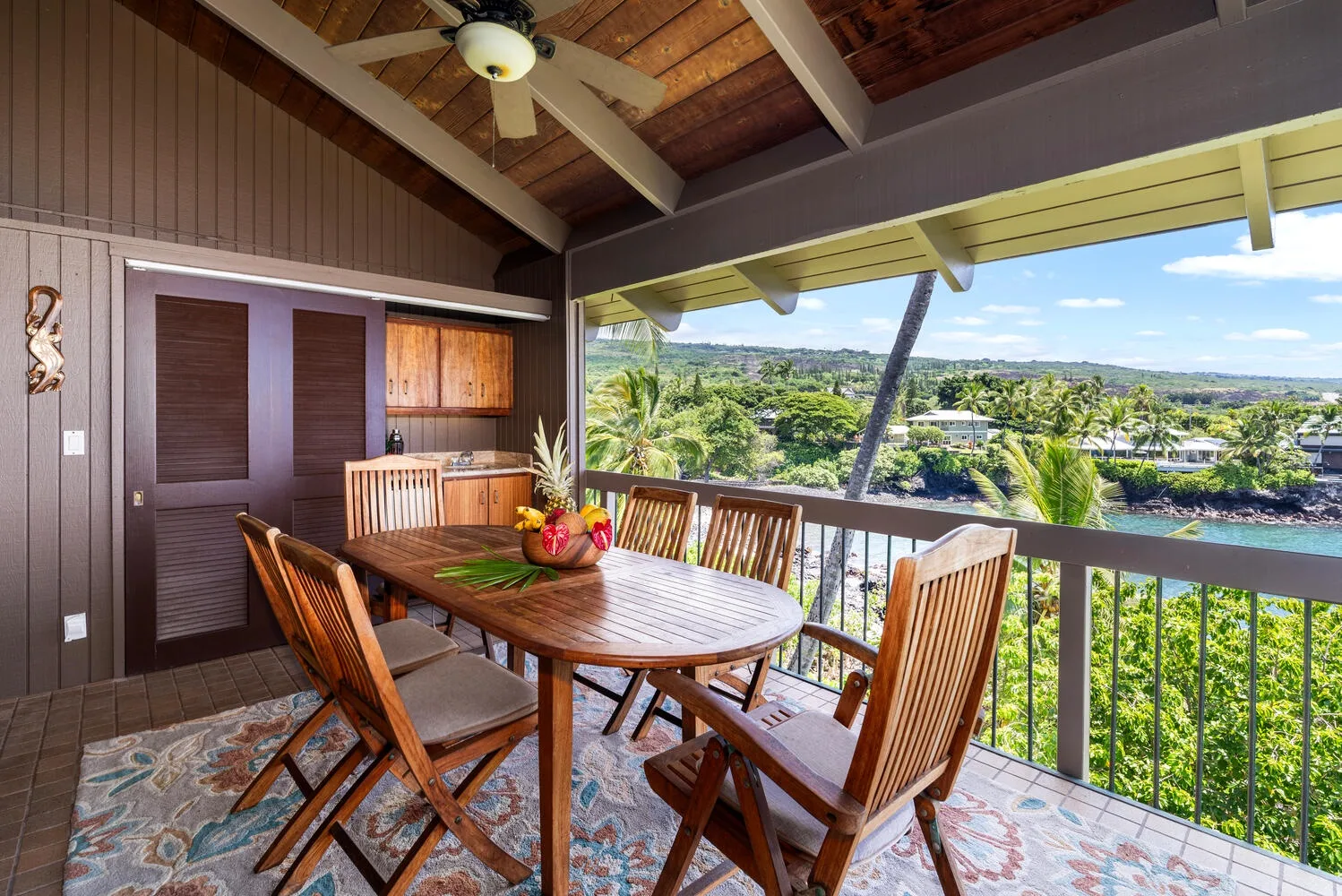 A covered outdoor dining area with a wooden table overlooks greenery and the water.