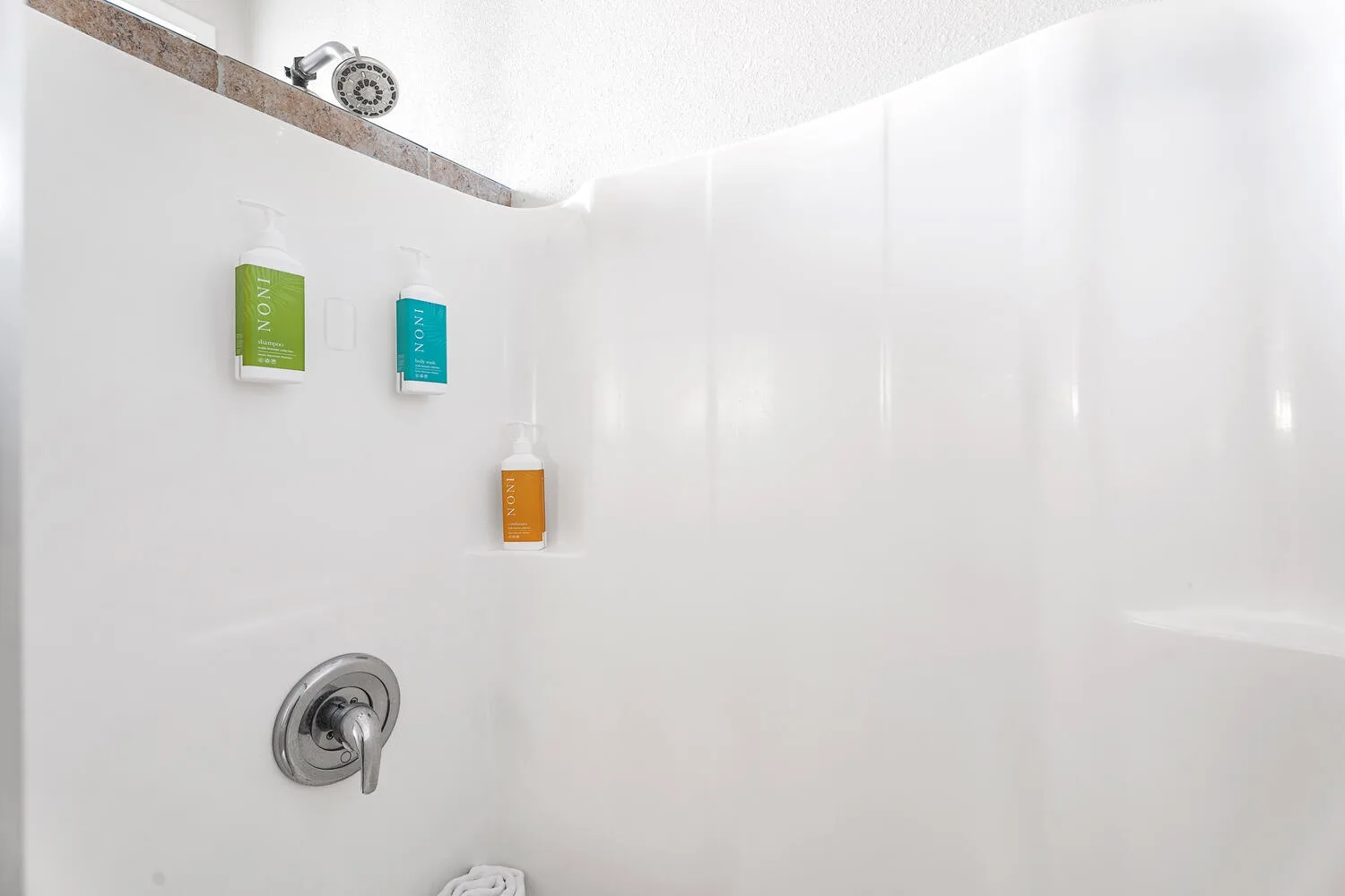 A white shower with a wall-mounted showerhead and control handle.