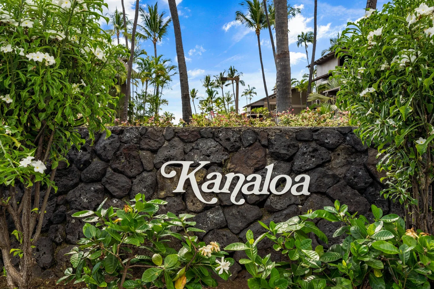 A landscaped tropical entrance features a stone wall with a Kanaloa sign.