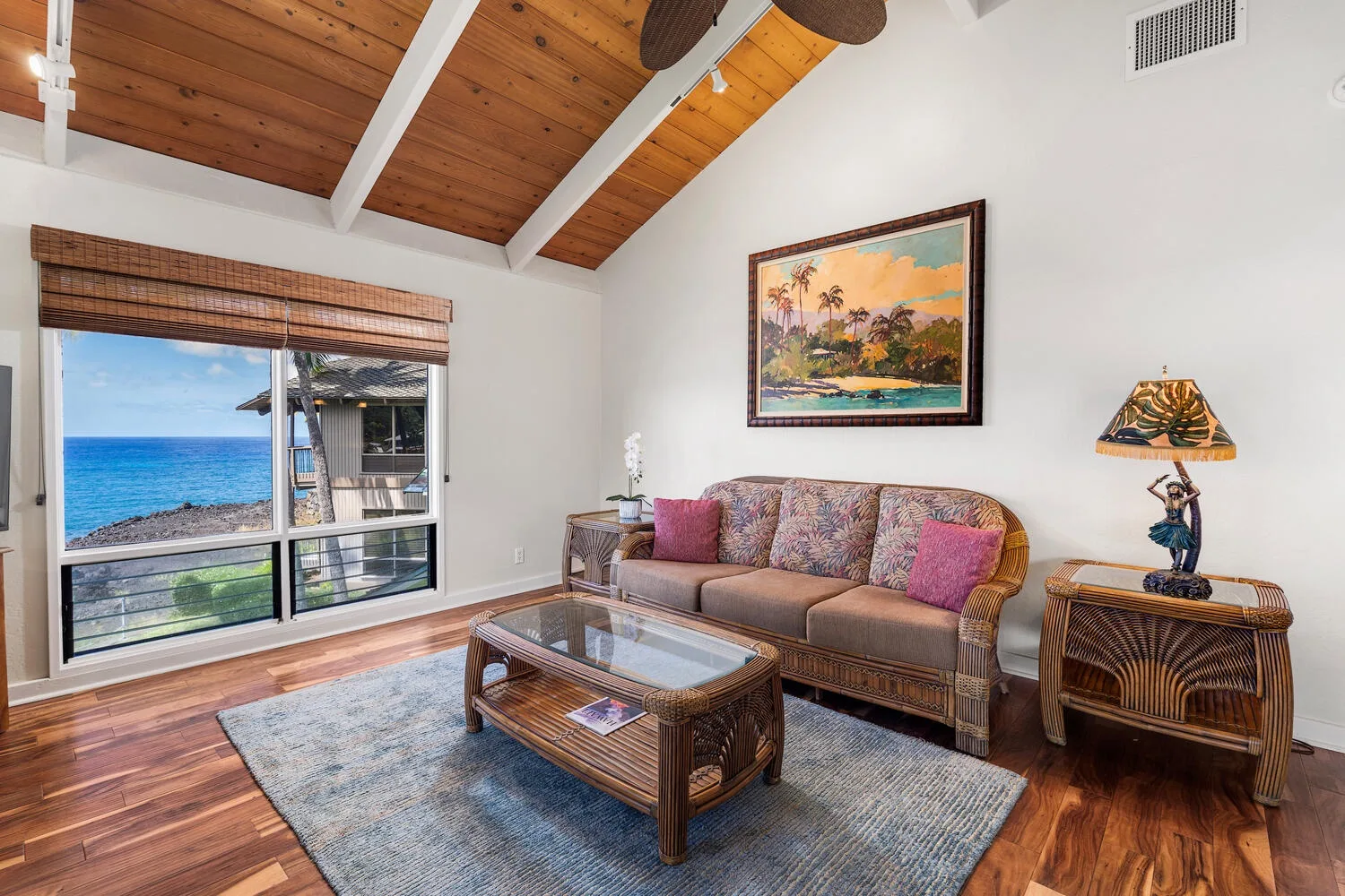 A living room with seating, a glass coffee table, and a large window overlooking the water.