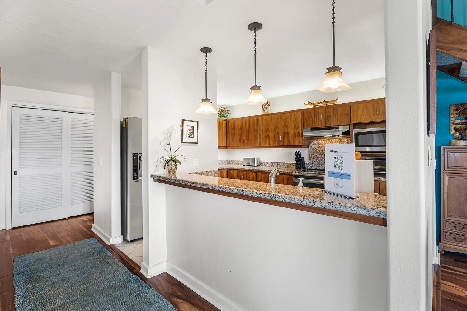 An open kitchen with a long counter, wooden cabinets, and pendant lights.