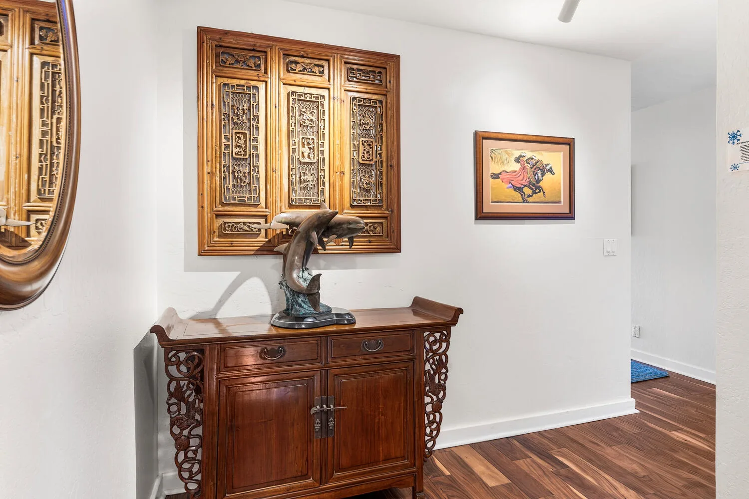 A hallway with a carved wooden cabinet, decorative sculpture, and framed artwork.