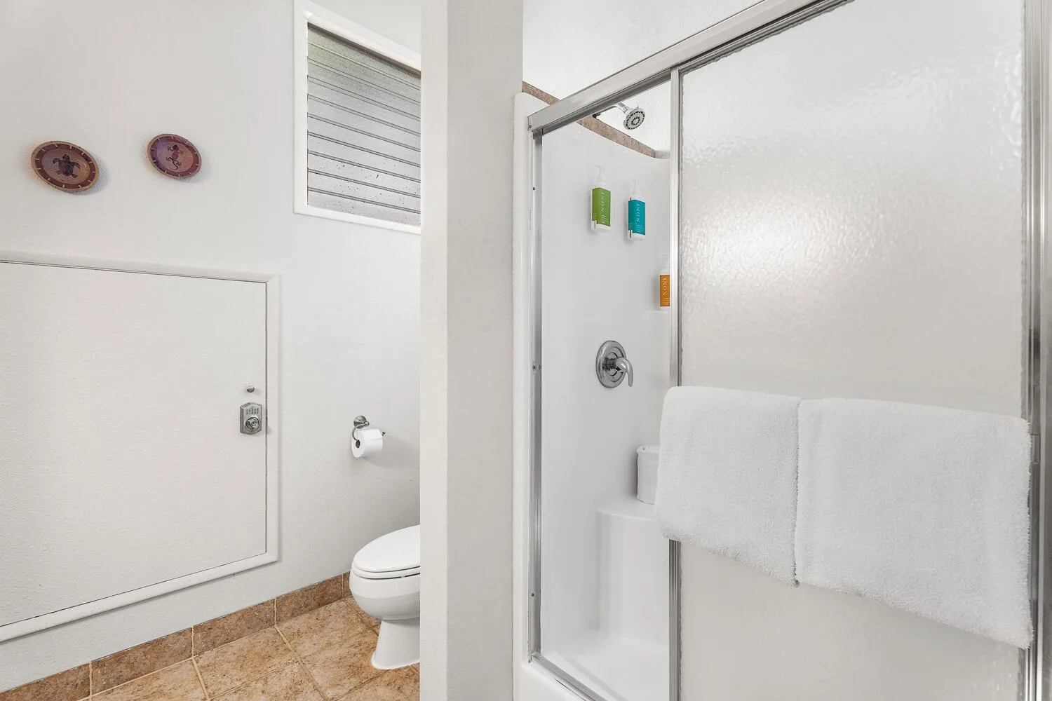 A bright bathroom with a glass shower, toilet, and folded towels.