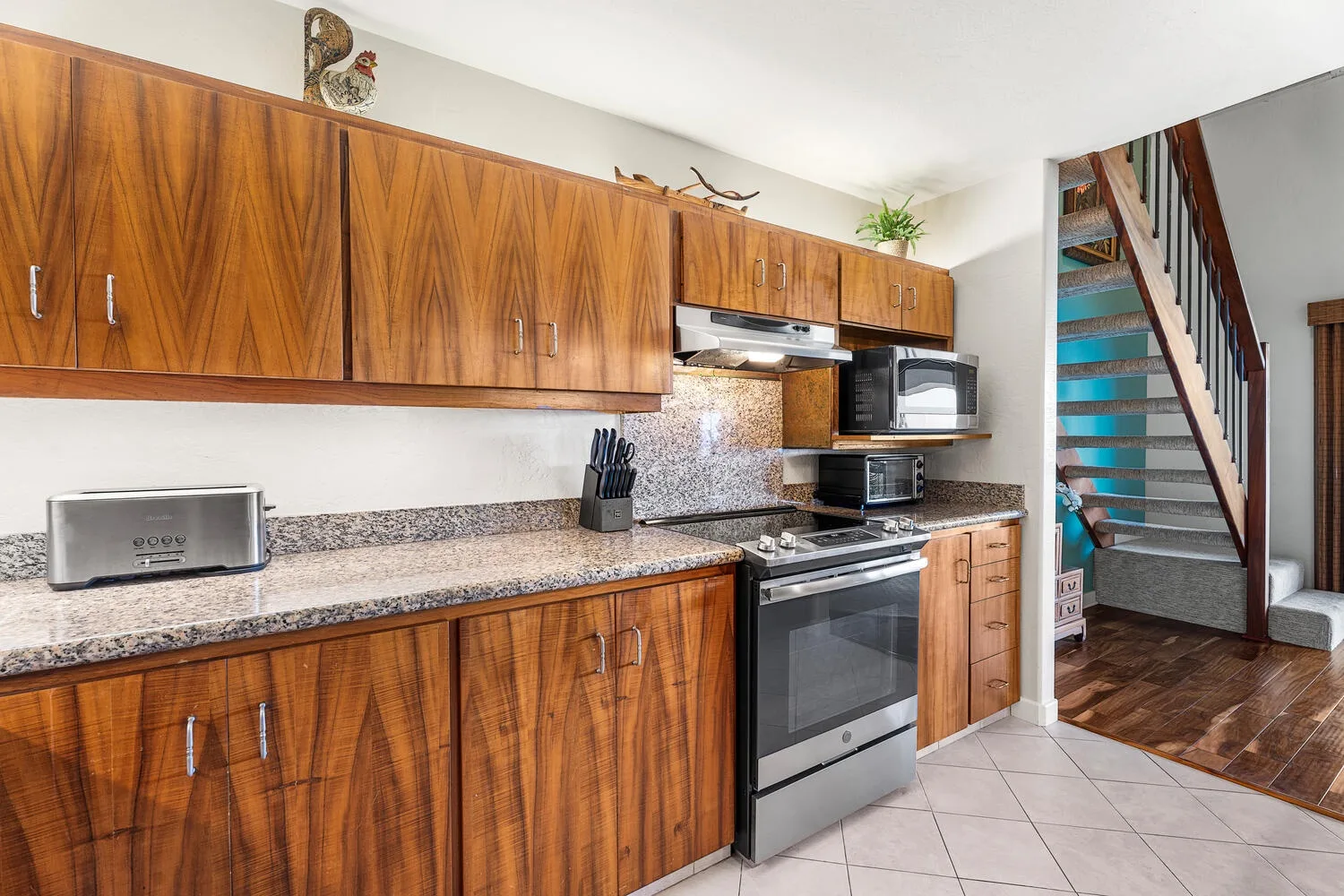 A kitchen with wooden cabinets, granite countertops, and a stove beside the stairs.