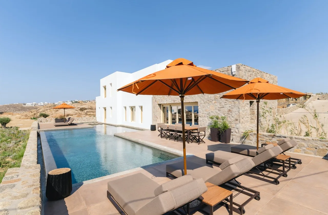 An outdoor pool beside a white building, with loungers and orange umbrellas.