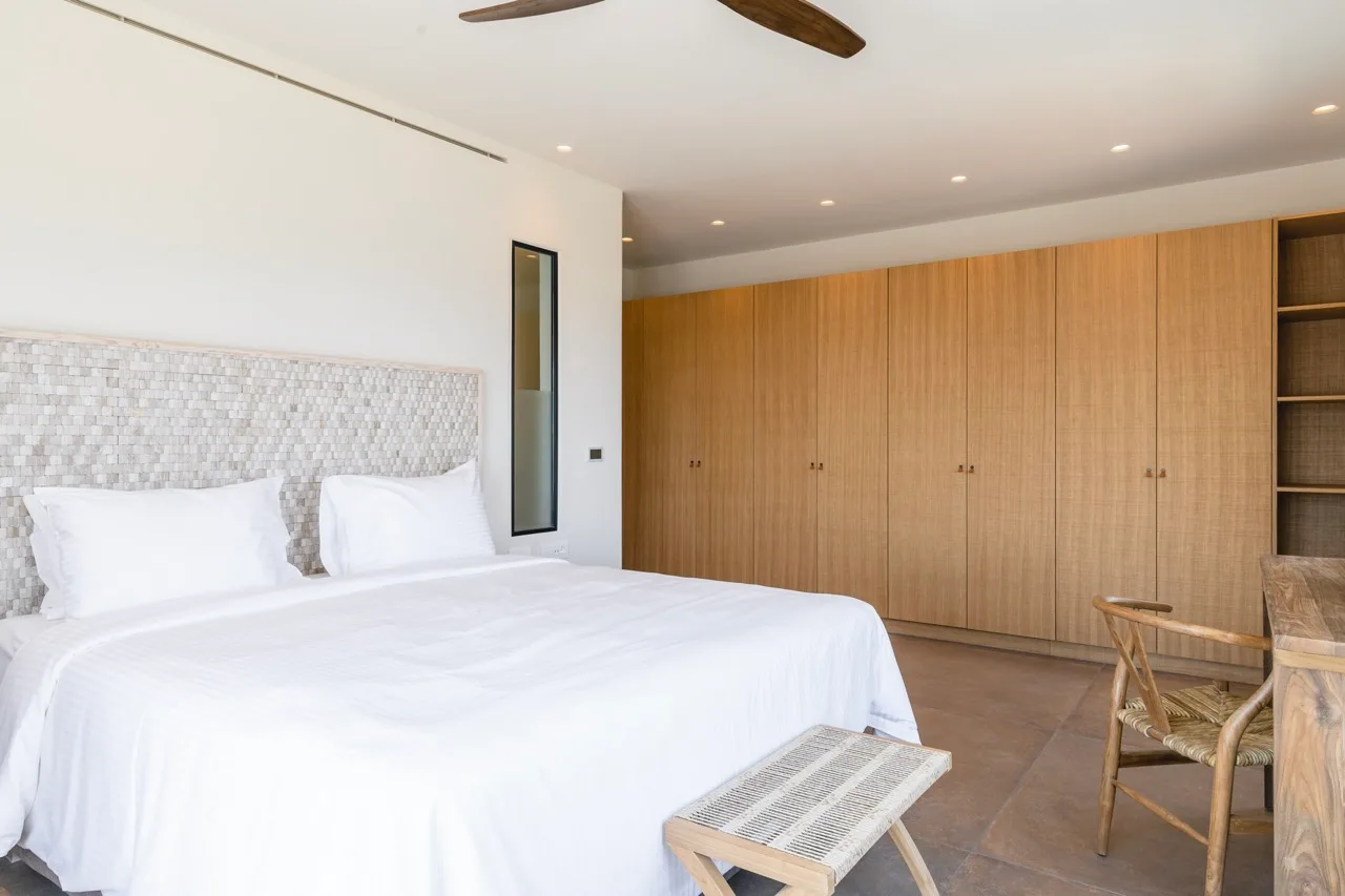 A bright bedroom with a white bed and wall of wooden cabinets.