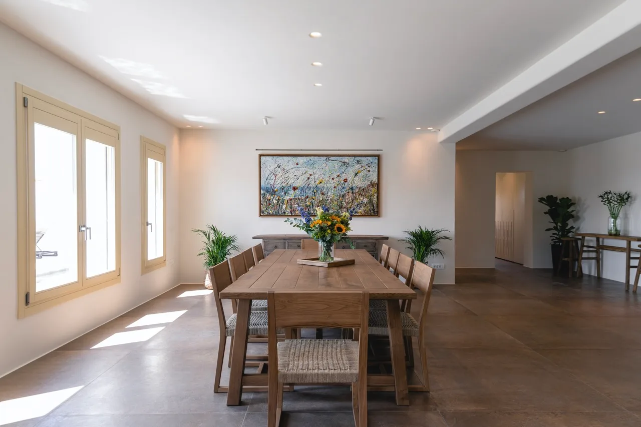 Dining room with a long wooden table and colorful artwork on the wall.