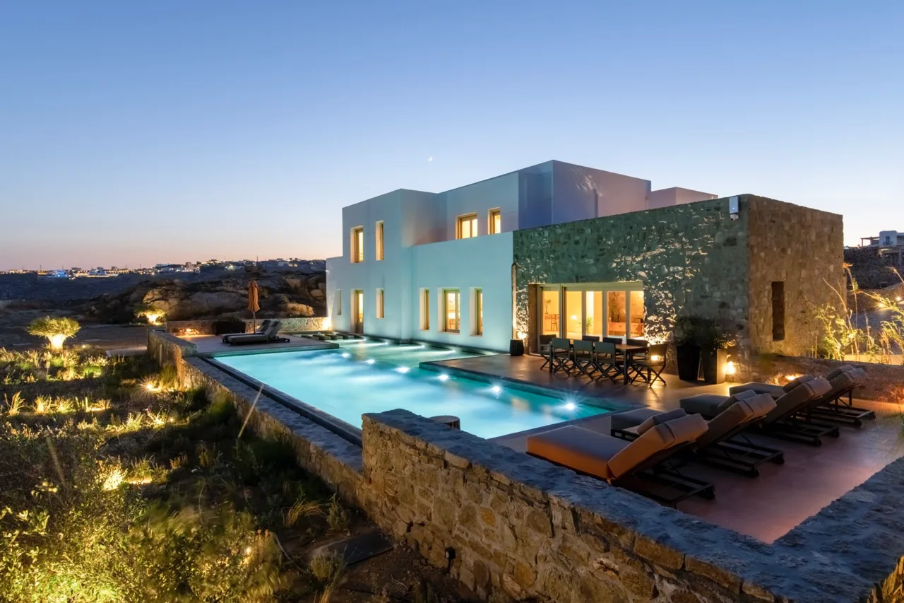 A modern villa beside a lit swimming pool at dusk.