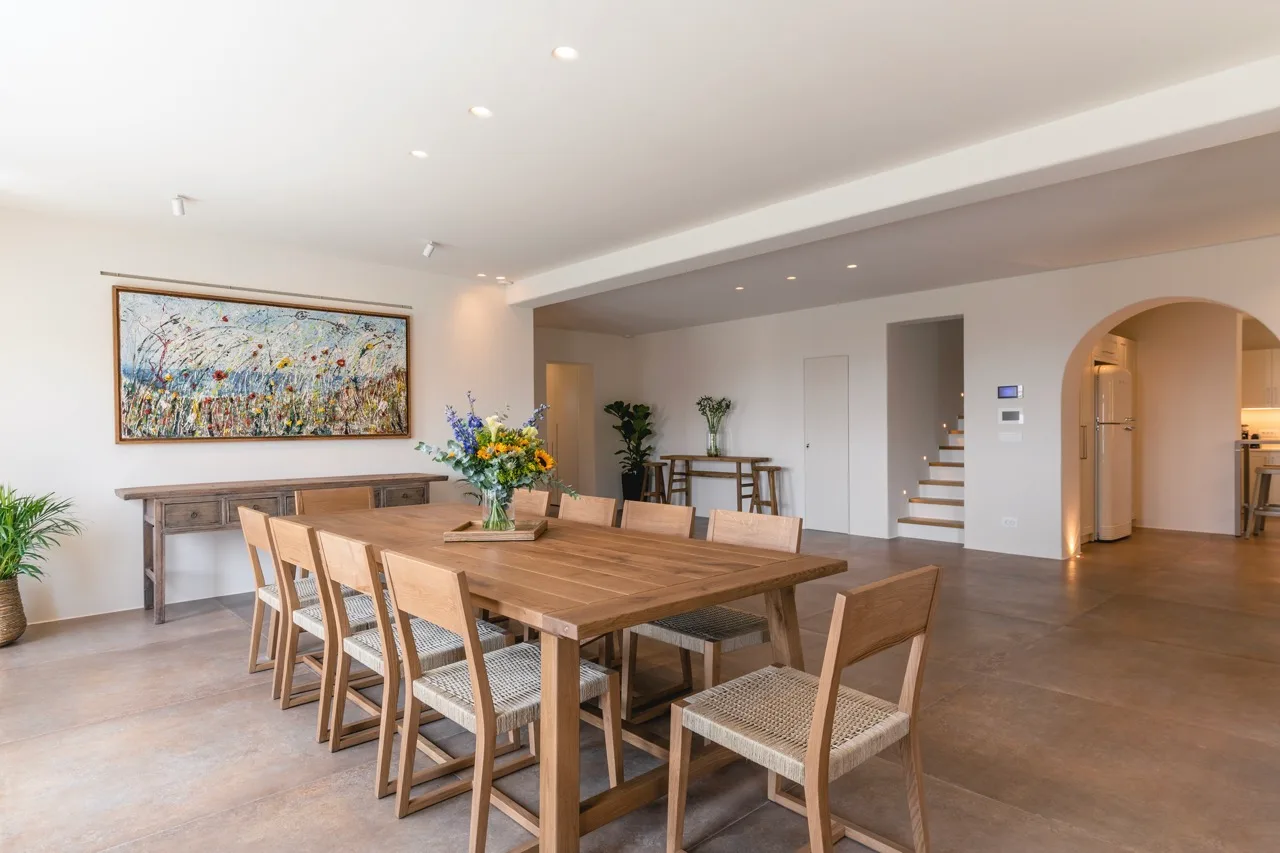 A dining area with a long wooden table and a large framed artwork on the wall.