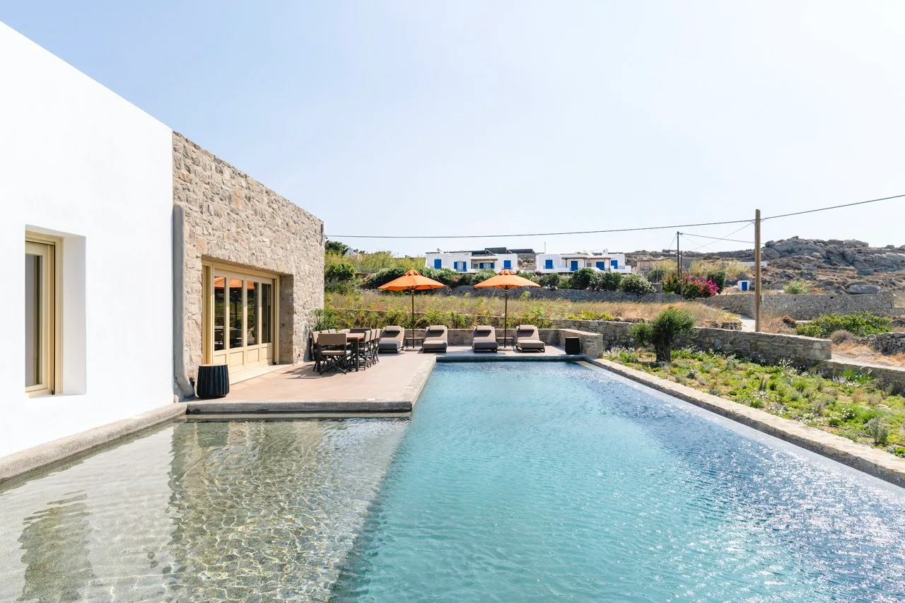 Outdoor swimming pool beside a modern building with seating and umbrellas.