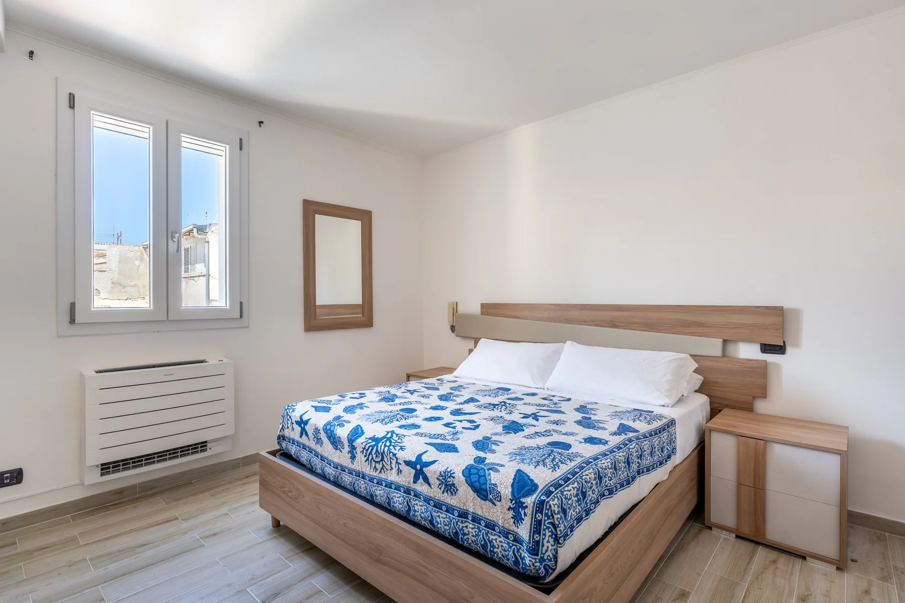 Un dormitorio luminoso con una cama vestida con ropa de cama estampada azul y blanca.