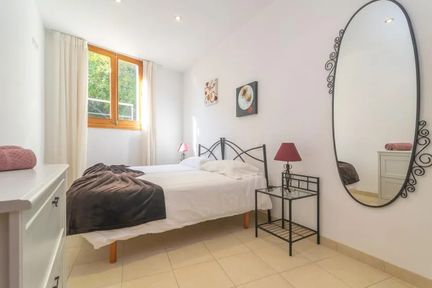 A bright bedroom with a bed, bedside tables, and a large oval mirror.