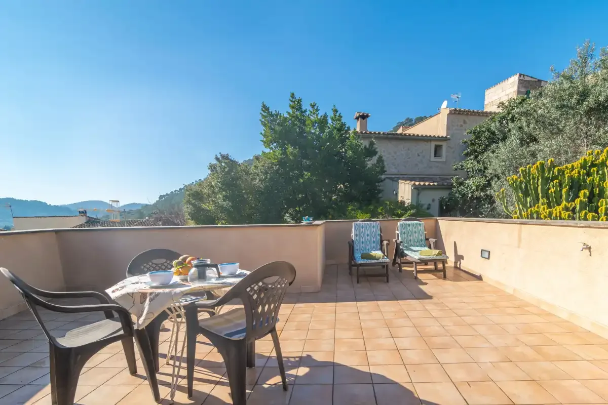 A sunny terrace has outdoor seating and views of nearby buildings and hills.