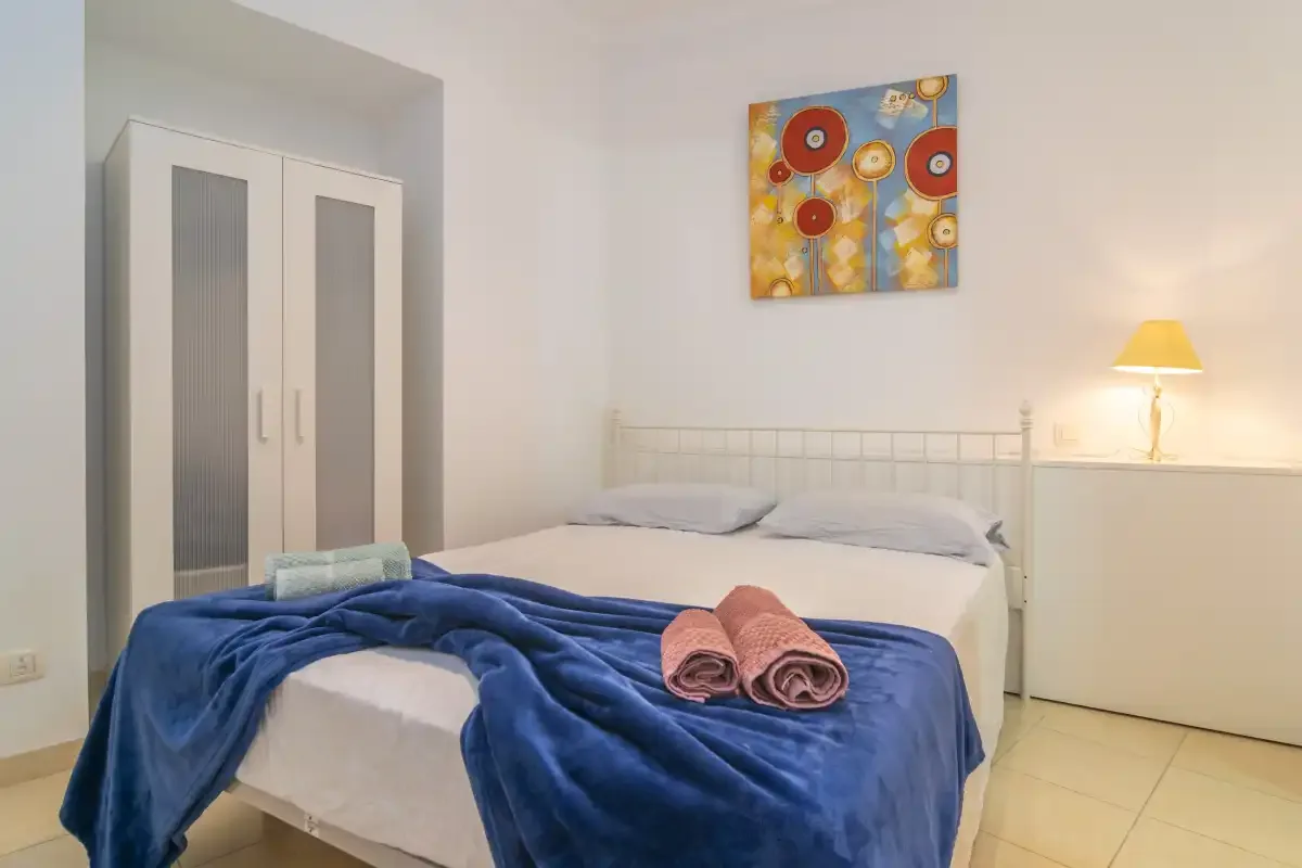 A bedroom with a neatly made bed, blue blanket, and bedside lamp.