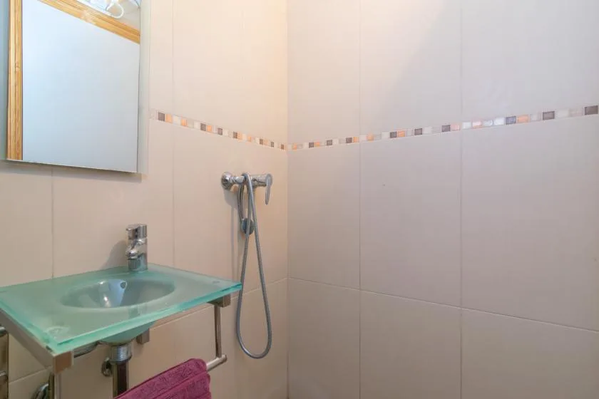 A tiled bathroom with a glass sink and wall-mounted shower.