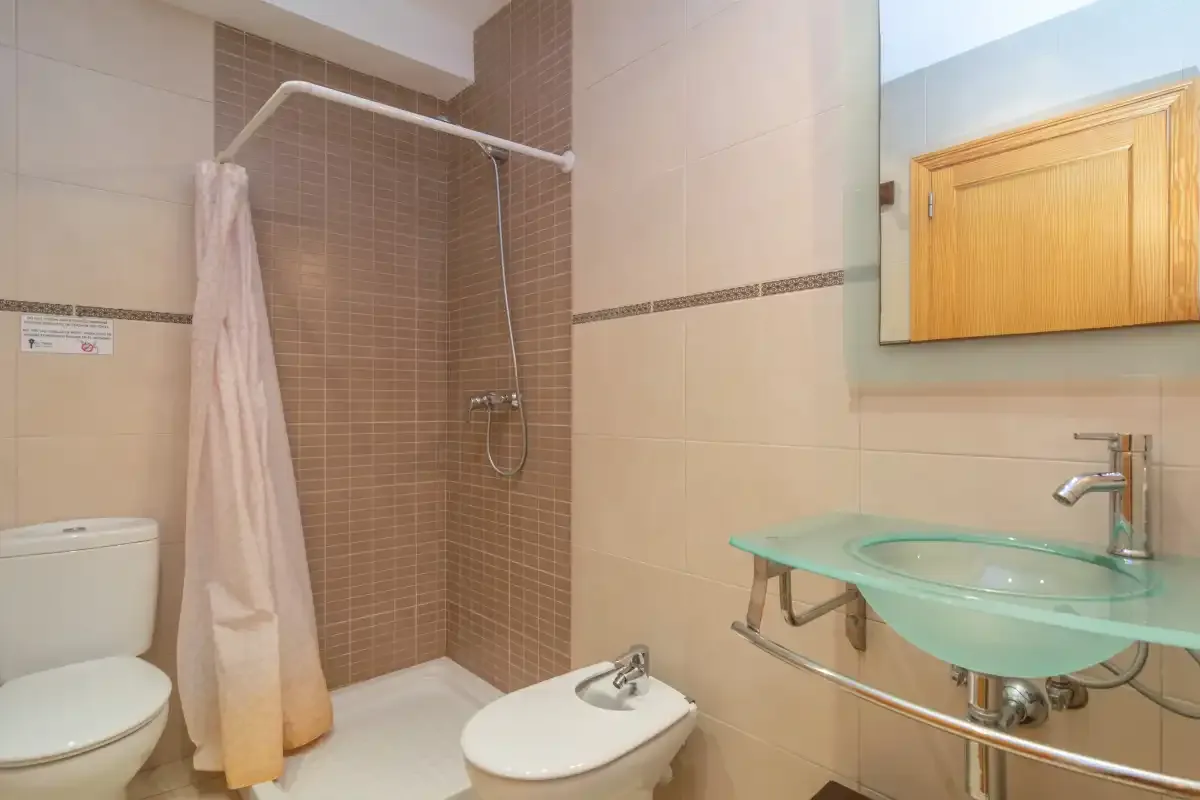 A tiled bathroom with a shower, toilet, and glass sink.