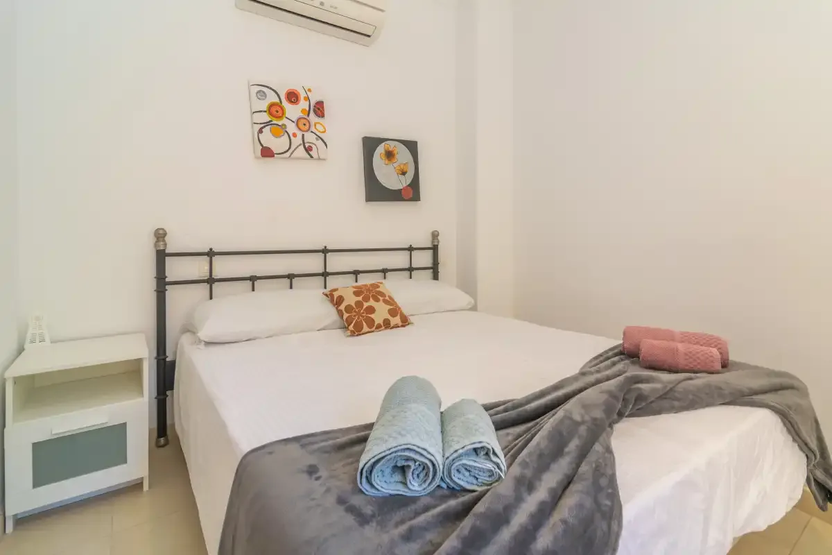 A bedroom with a bed, folded towels, and a gray blanket.