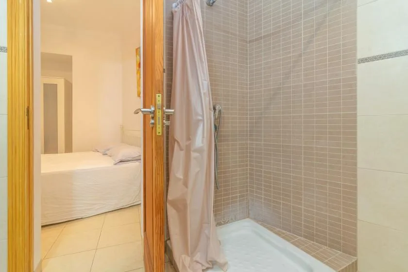 A tiled bathroom with a shower beside an open doorway to a bedroom.