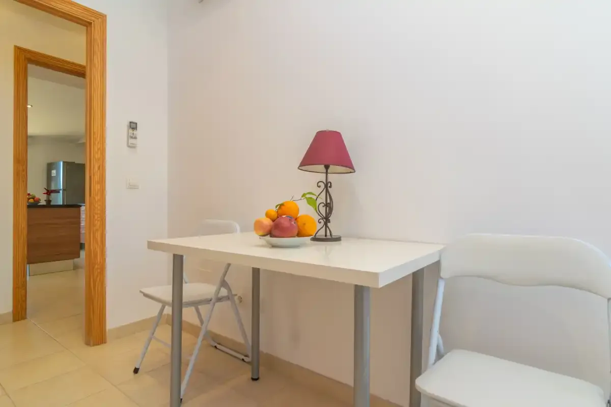 A dining area with a white table, fruit, and a lamp.