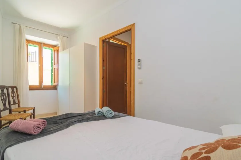 A bedroom with a bed, wooden chairs, and a bright window.
