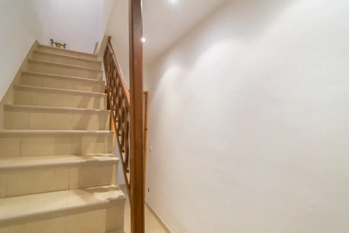 A tiled staircase with a wooden railing beside a plain white wall.