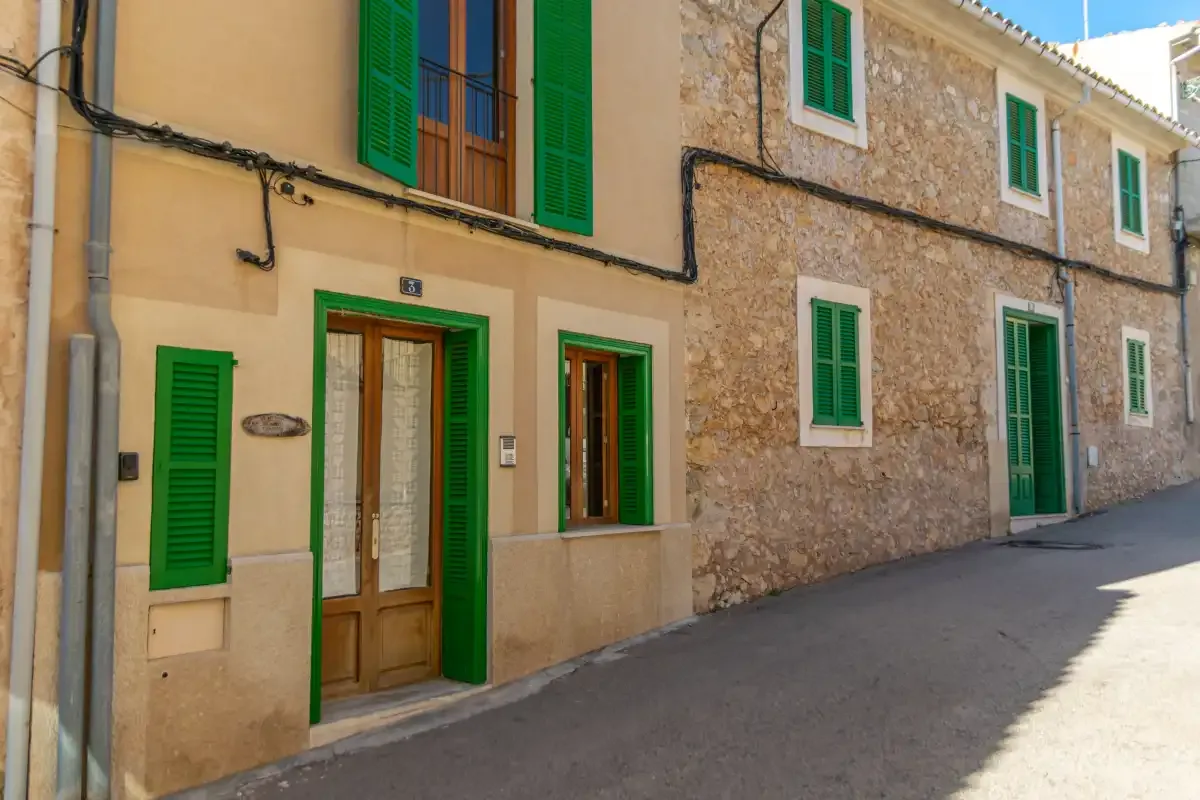 A row of village houses with green shutters faces a narrow paved street.