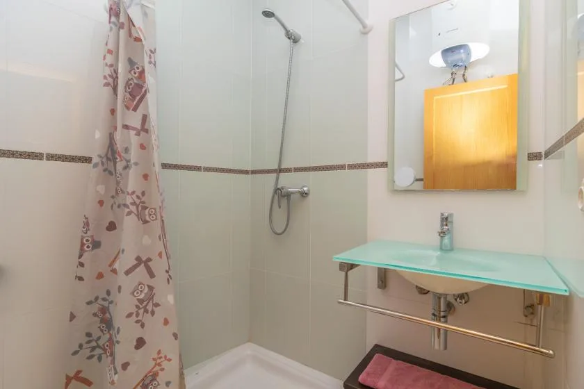 A tiled bathroom with a shower, patterned curtain, and glass sink shelf.