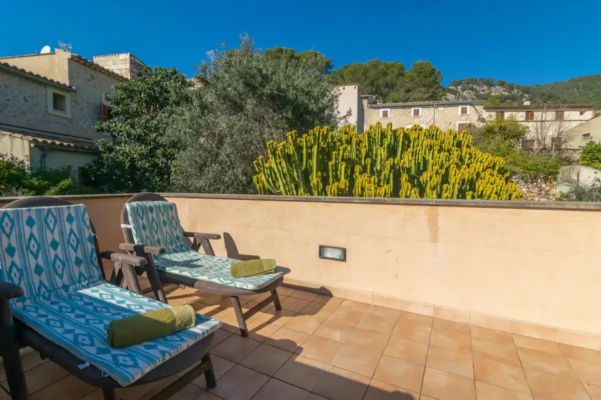 A sunny terrace with cushioned seating overlooks a cactus and nearby buildings.