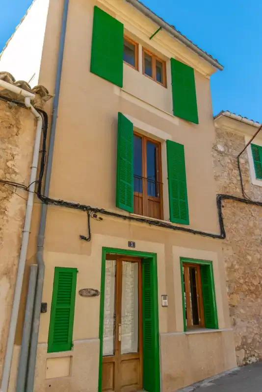 A narrow multistory house facade has green shutters around its windows.