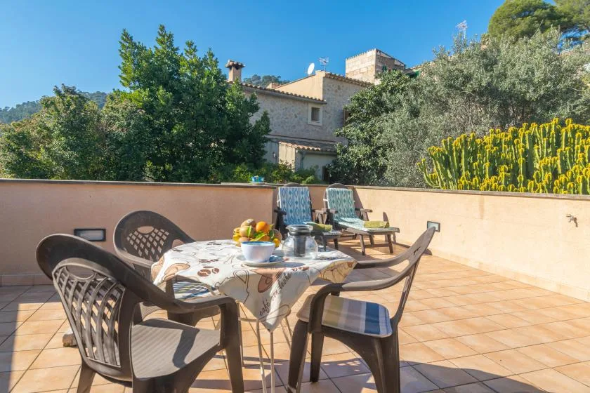 An outdoor terrace with a dining table and seating overlooks leafy greenery.